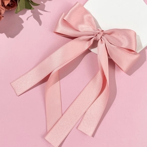Close-up of pink satin bow hair clip with long ribbons showing soft silk texture