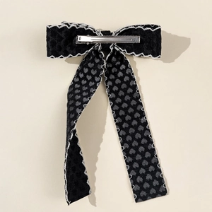 Détail d'une pince à cheveux à nœud noir avec bords ondulés et motifs de cœurs