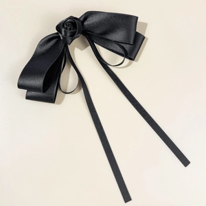 Detail of a black satin bow hair clip with a handmade rose and long elegant ribbons