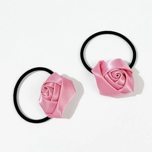 Détail de deux chouchous roses en forme de rose avec élastiques noirs sur fond blanc