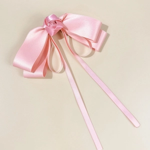 Elegant pink satin ribbon bow hair clip with center rose floral detail on beige surface