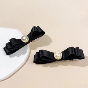Détail de barrettes à nœuds en satin noir avec perle et sertissage en chaîne dorée