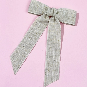 Close-up of champagne tweed bow hair clip with elegant long ribbons on pink background