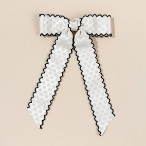 Détail d'un nœud en satin blanc avec bordure brodée ondulée noire pour accessoire cheveux