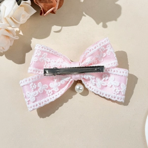 Detailed view of pink lace bow hair clip with white pearl pendant and metal alligator grip