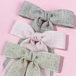 Three elegant vintage linen bow hair clips in grey and pink, layered on a pink surface