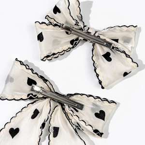 Detail of white mesh bow hair clips with black heart pattern and metal duckbill clip