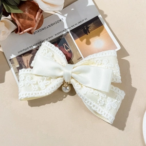 Detail of a creamy lace and satin bow hair clip with a delicate pearl pendant accent