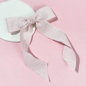 Pink ribbon bow hair clip with textured fabric on a minimalist white display plate