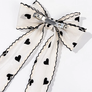 Detail of white mesh bow hair clip featuring black heart prints and silver metal spring clip