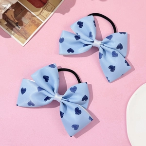 Détail de chouchous nœuds bleu clair avec motifs cœurs bleus sur un fond rose pastel