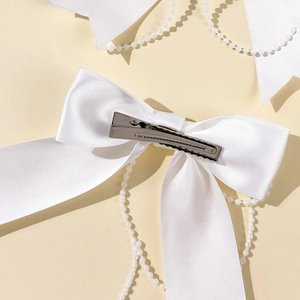 Detail of white satin bow hair clip with faux pearl fringe and silver duckbill metal clip