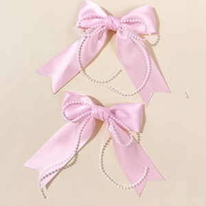 Detail view of two soft pink satin bow hair clips with delicate white faux pearl chains