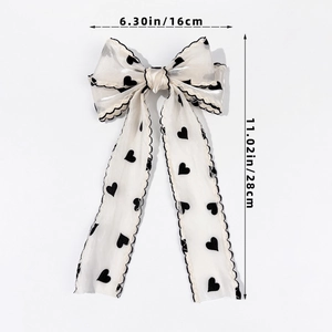 Detail view of a cream mesh bow hair clip featuring black heart patterns and wavy edges