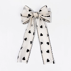 Detail of a mesh hair bow clip with black heart patterns and wavy stitched edges