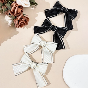 Set of black and beige bow hair clips with delicate fabric texture on a cream background