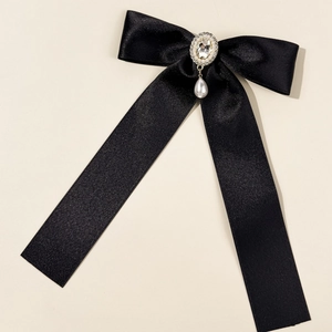 Detailed close-up of a black satin bow hairpin with pearl drop and crystal embellishment