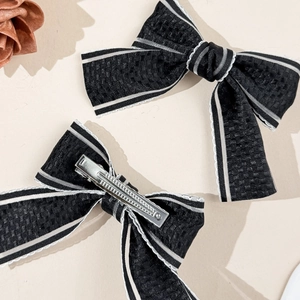 Close-up of black plaid ribbon bow hair clip with silver metal duckbill clip detail