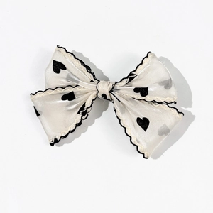 Detail of a beige mesh bow hair clip with black heart patterns and wavy edges