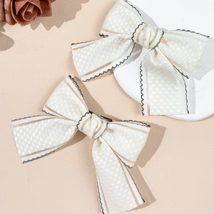 Elegant cream bow hair clips with black scalloped edges and textured fabric pattern