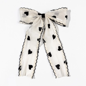 Detailed close-up of cream bow hair clip with black heart prints and wavy scalloped edges