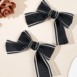 Detailed macro view of two black bow hair clips with white stripes and waffle texture