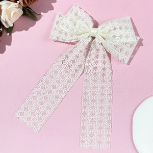 Détail d'un nœud papillon en dentelle blanche avec de longs rubans sur fond rose