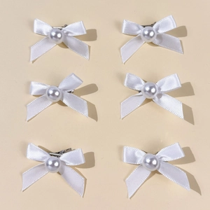 Lot de six barrettes à nœuds blancs avec perles montrées en détail sur fond jaune doux