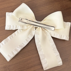 Vista posteriore di un fermaglio per capelli a fiocco crema con bordi a balze e clip a becco d'anatra