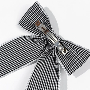 Détail de la pince métallique argentée et du nœud en tissu à carreaux noir et blanc