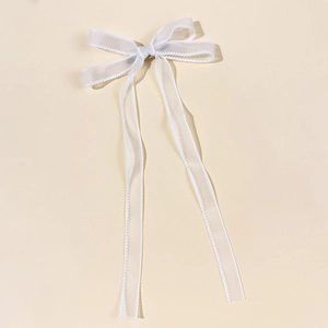 Détail de la pince à cheveux nœud en mousseline blanche avec bordure perlée et longs rubans