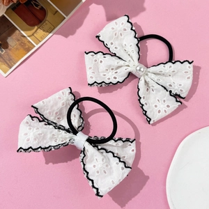Detailed close-up of white lace bow hair ties with pearl accents on a soft pink background