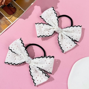 Detail of white lace bow hair ties with pearl accents and black embroidery on pink backdrop