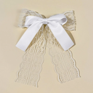 Detail of elegant white lace bow hair clip with ribbons on a clean beige background