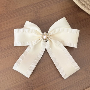 Dettaglio molletta a fiocco color crema con perla e strass su superficie in legno