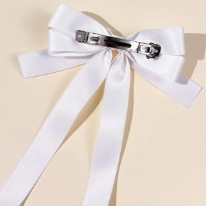 Close-up of white satin bow hair clip showing the silver metal spring fastener detail