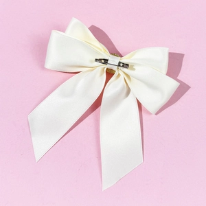 Detail of cream satin bow brooch with silver metal clip on pink textured background