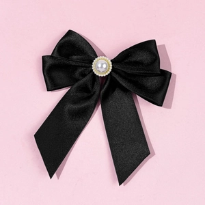Detail of a black satin bow brooch with an elegant central pearl and gold trim