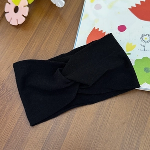 Close-up of a black elastic twisted knot headband on a wooden surface with lifestyle props