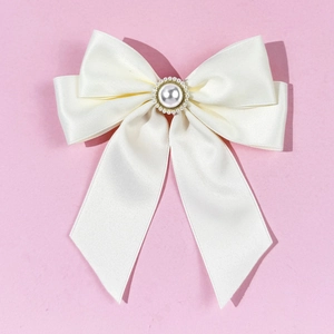 Close-up of cream satin bow brooch featuring a large pearl and gold rhinestone center