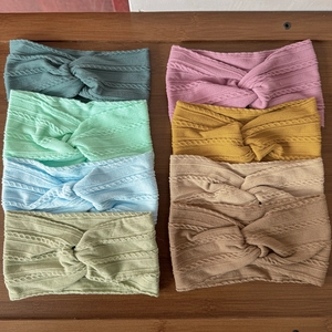 Knitted ribbed baby headbands in seven pastel colors on a rustic wooden background