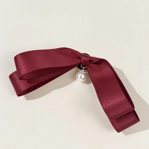 Close-up of a burgundy satin bow accessory featuring a delicate white faux pearl pendant