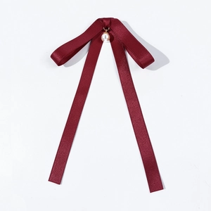 Macro shot of a wine red satin bow tie featuring a white pearl pendant and long ribbons