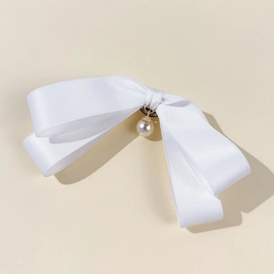 Detailed view of a white silk bow accessory with a pearl pendant and golden metal base