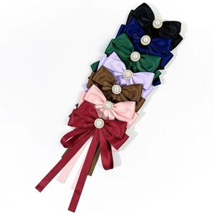 Close-up of satin bow brooches with faux pearls and long ribbons in seven elegant colors