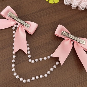 Detail van roze satijnen haarstrik met witte parelketting en zilveren metalen clip