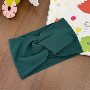 Detail of a dark green elastic cross-knot baby headband on a rustic wooden background