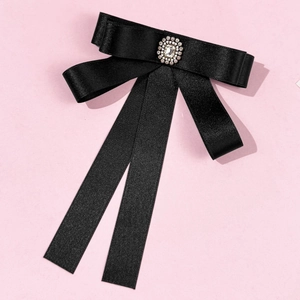 Detail of a black satin bow brooch with a central rhinestone centerpiece on pink background