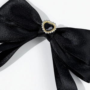 Detail of a black satin bow with heart-shaped gemstone and crystal trim on fabric