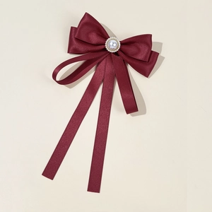 Detailed view of a wine red satin bow brooch with an elegant pearl and rhinestone center
